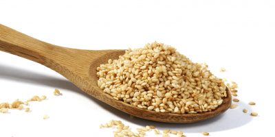 Sesame grains in large wooden spoon on white background